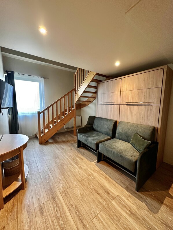 A room with a wooden staircase, a sofa, a TV, and a wooden floor.