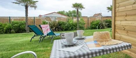 A checkered table with cups and a hat, surrounded by a wooden fence and greenery.