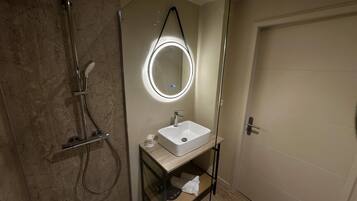 Une salle de bain moderne avec une douche à parois de verre, un miroir rond et un lavabo blanc.