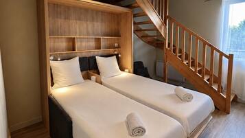 Une chambre avec deux lits, une tête de lit en bois, un escalier et une fenêtre.
