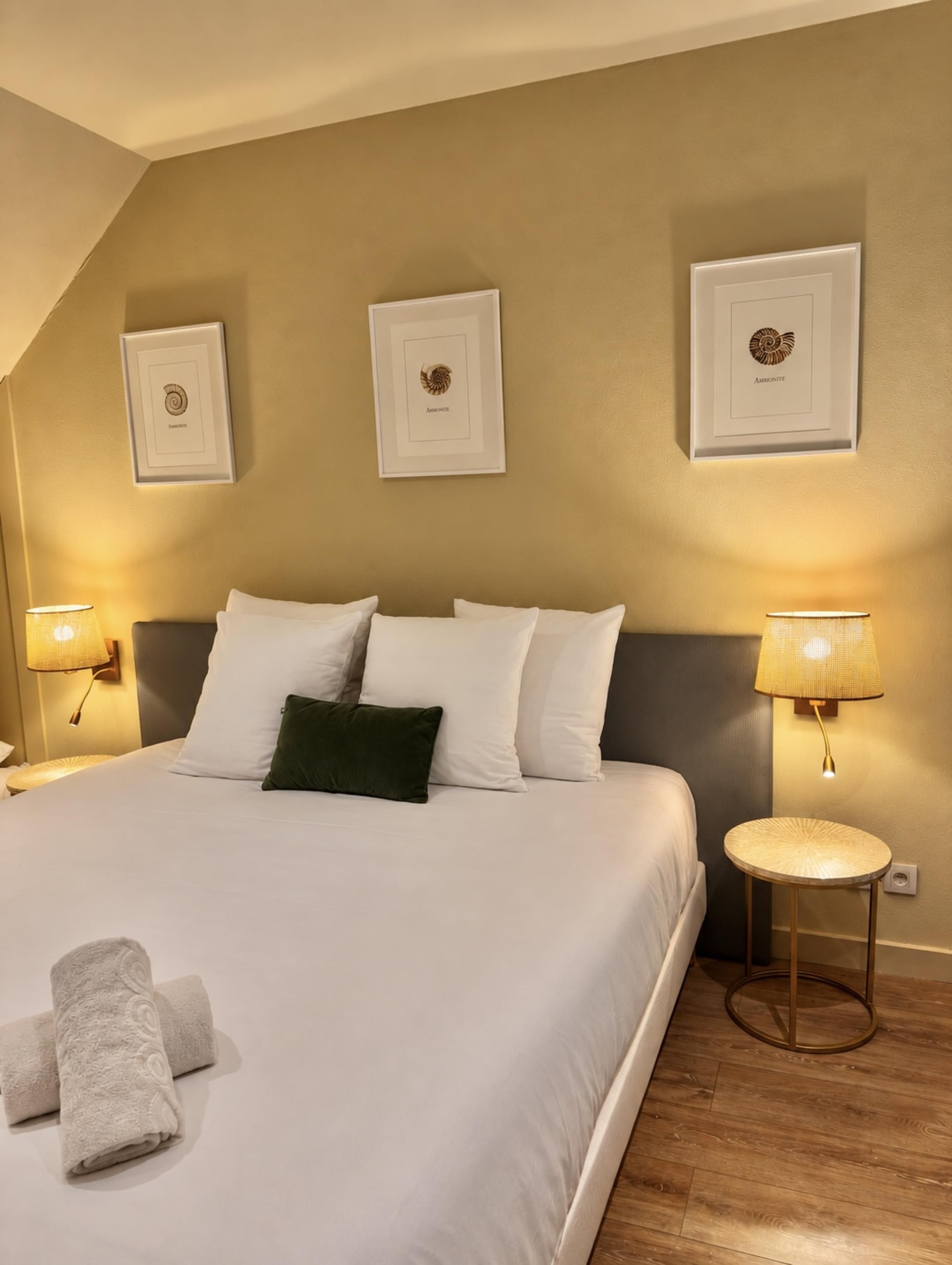 A hotel room with a large bed, two wall-mounted lamps, and three framed pictures on the wall.