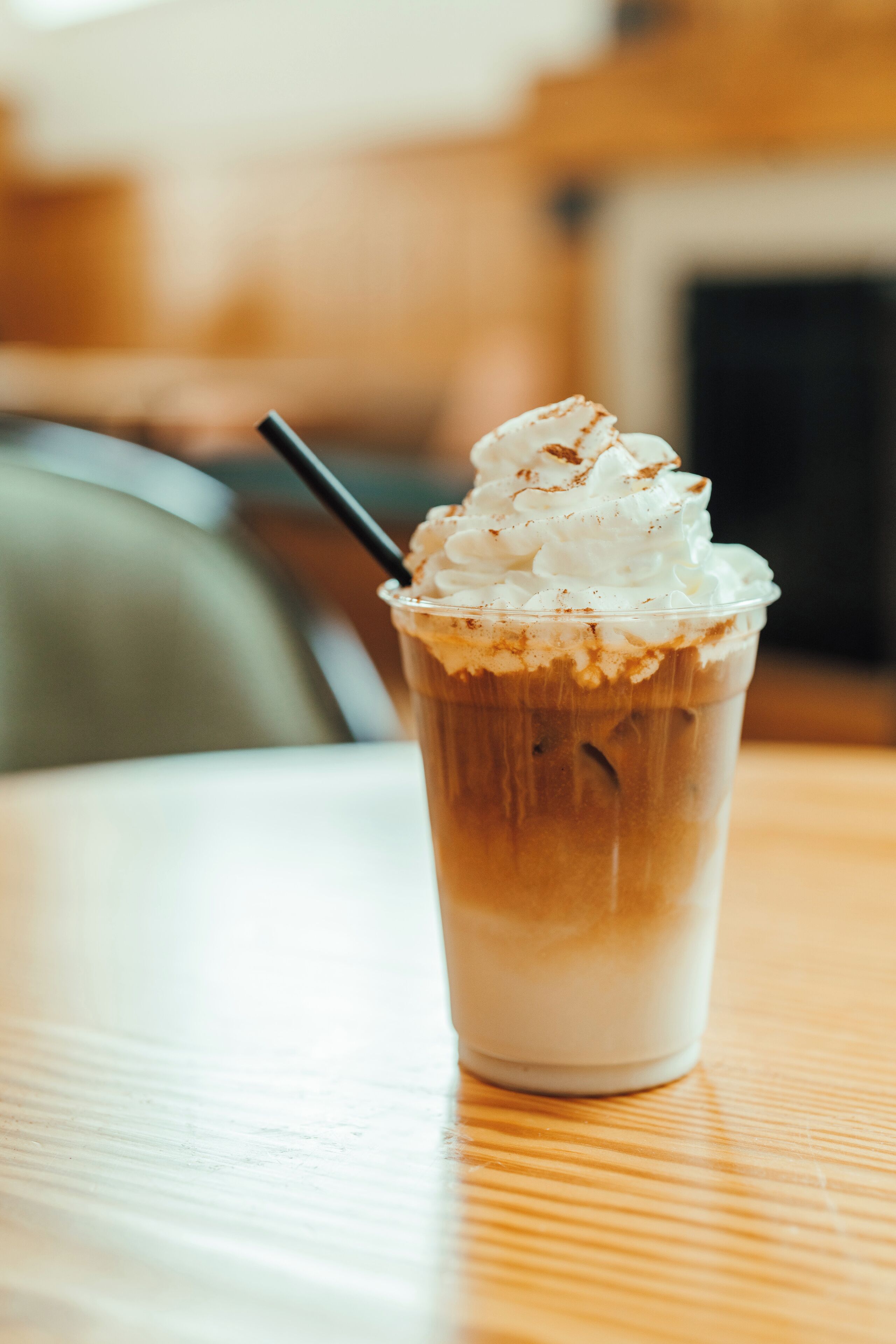 A clear glass of iced coffee with whipped cream and a sprinkle of cinnamon on a wooden table.