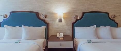 A hotel room with two beds, each with a headboard, a bedside table, a lamp, and a phone.