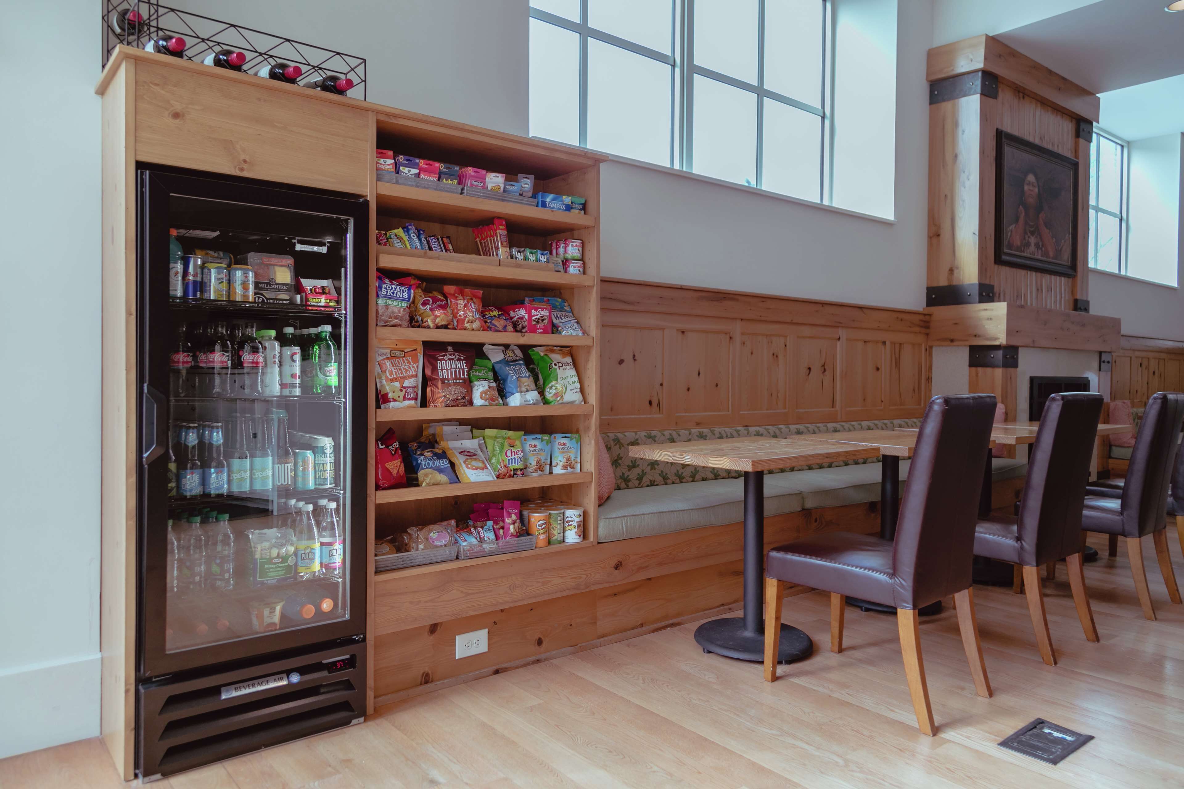 A dining area with a wooden bench, a built-in refrigerator stocked with beverages and snacks, and a wooden wall with shelves holding various food items.