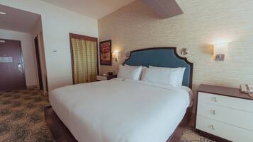 A hotel room with a large bed, a nightstand with a lamp, and a wall-mounted light.