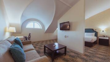 Een hotelkamer met een gebogen plafond, een aan de muur bevestigde televisie, een bed met witte beddengoed, een klein tafeltje en een kamerbreed tapijt met dessin.