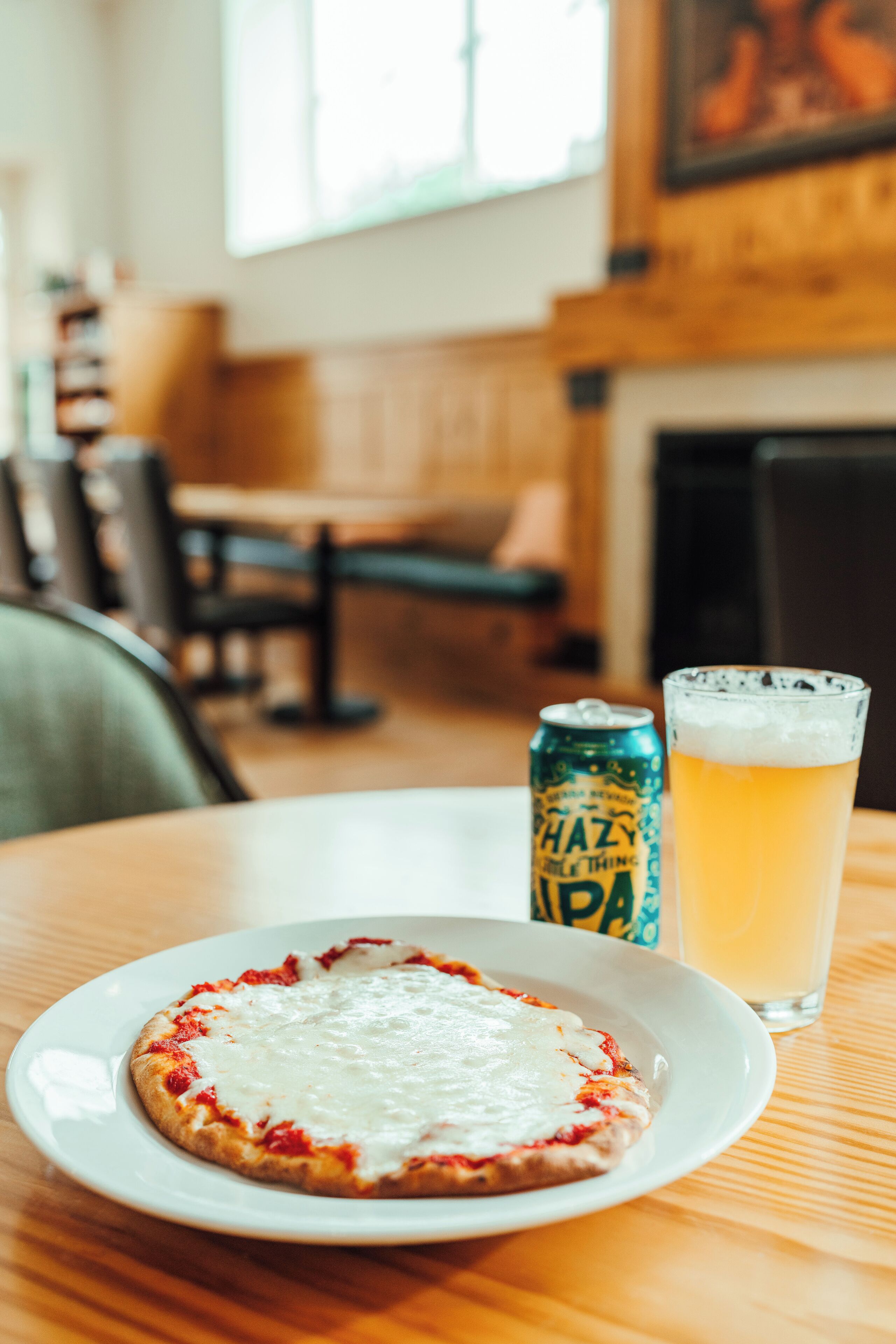 A pizza on a white plate with a can of beer and a glass of beer on a wooden table.