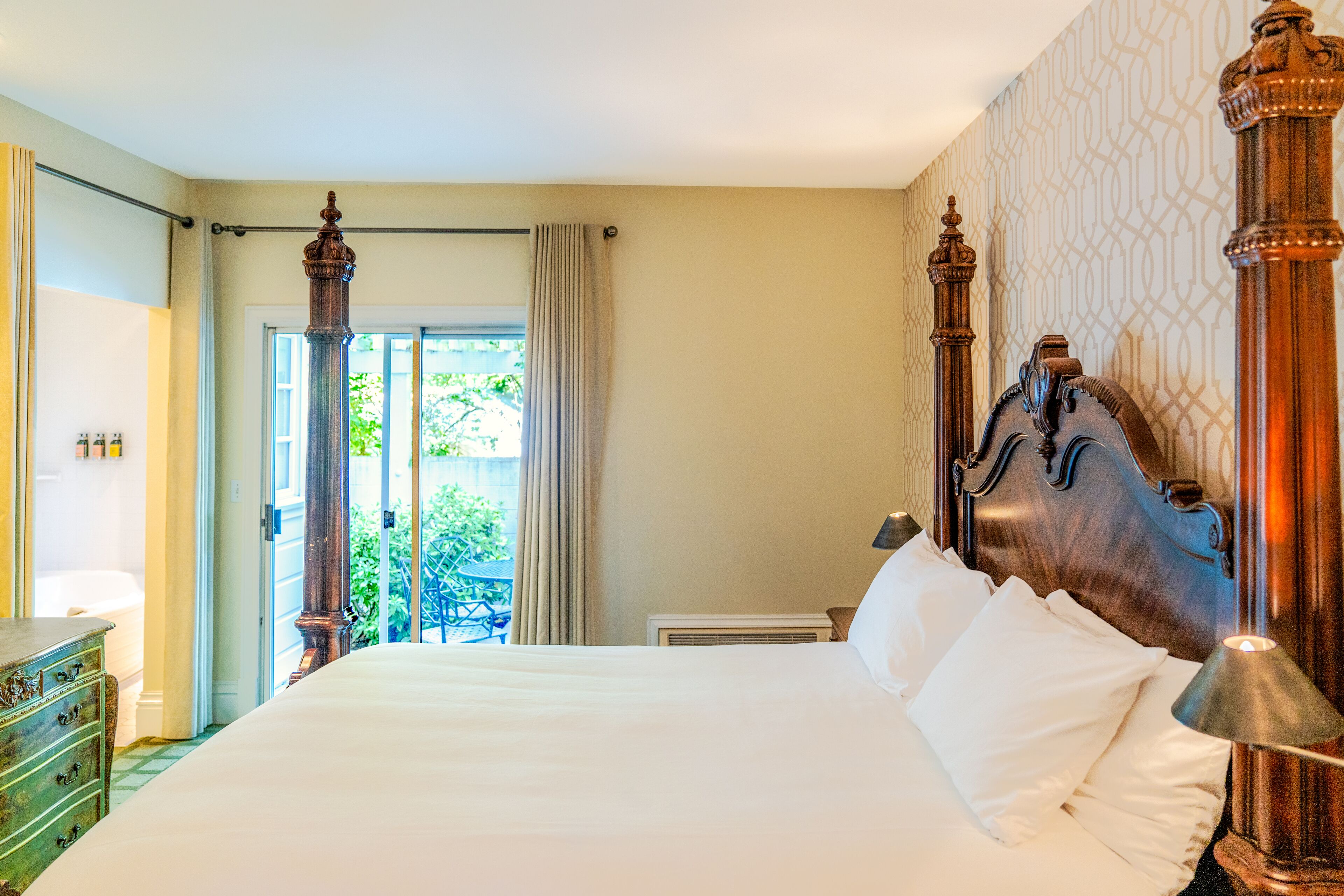 Una cama grande con cabecera de madera, un aparador y vistas del exterior a través de un ventanal.