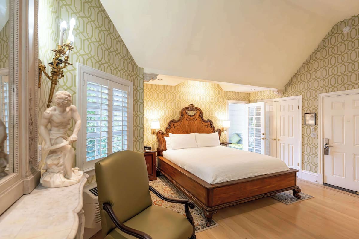 A bedroom with a wooden bed, a chair, a statue, and patterned wallpaper.