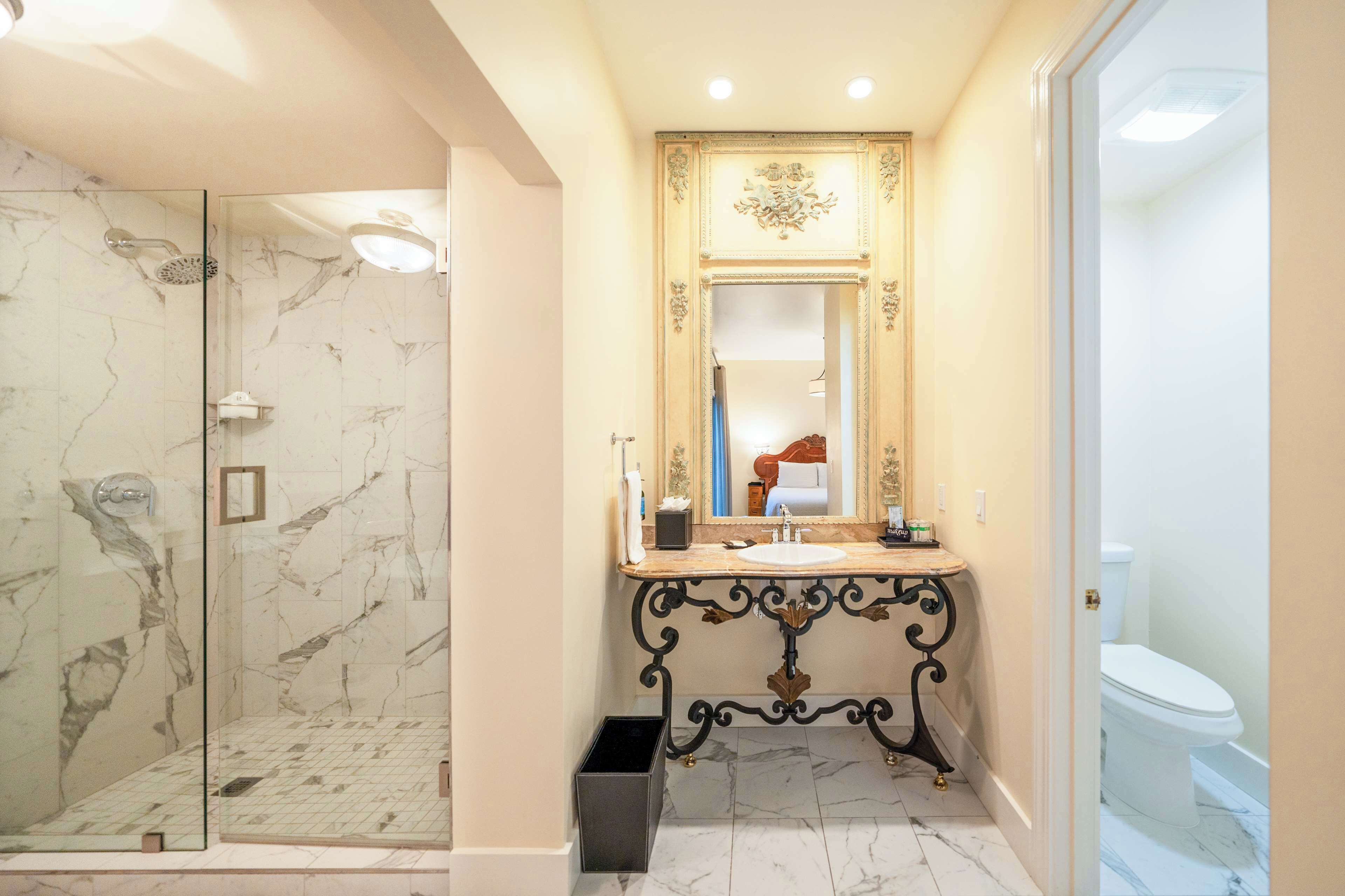A bathroom with a glass-enclosed shower, a marble-tiled floor, a vanity with a mirror, and a toilet.