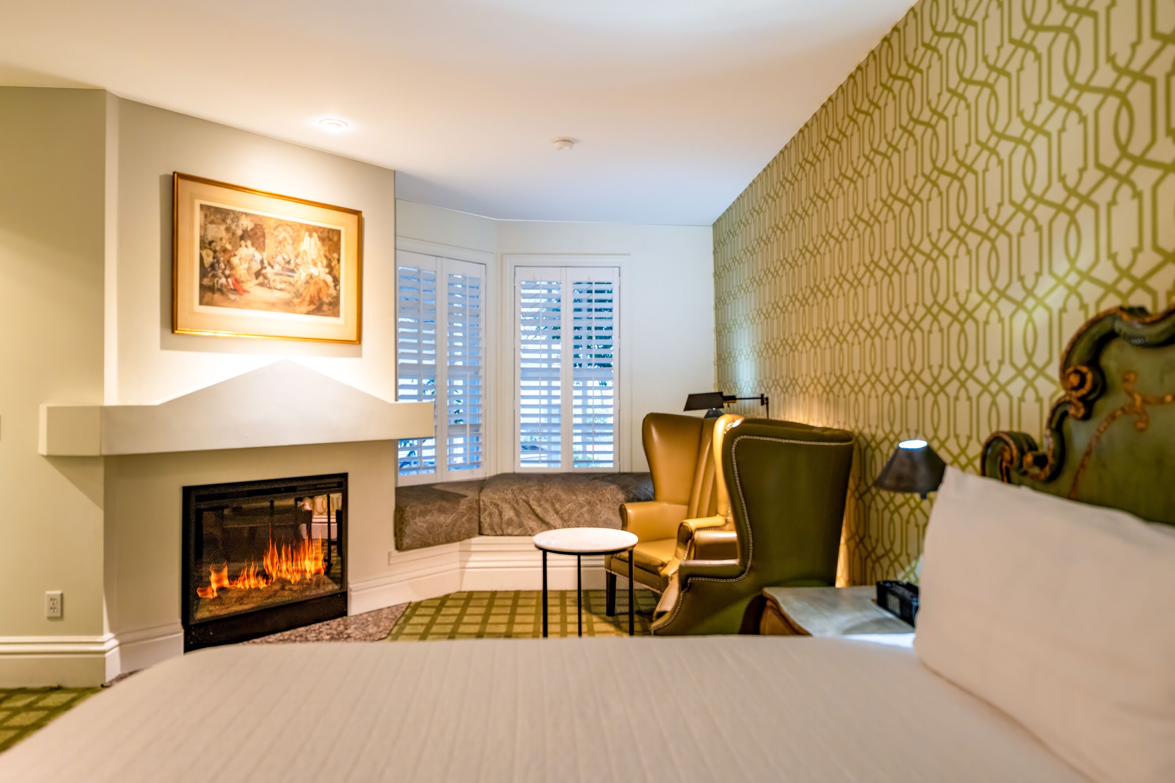 Habitación de hotel con chimenea, una cama grande, una zona de estar con una silla y un cuadro en la pared.