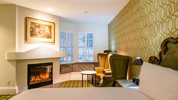 Habitación de hotel con chimenea, una cama grande, una zona de estar con una silla y un cuadro en la pared.