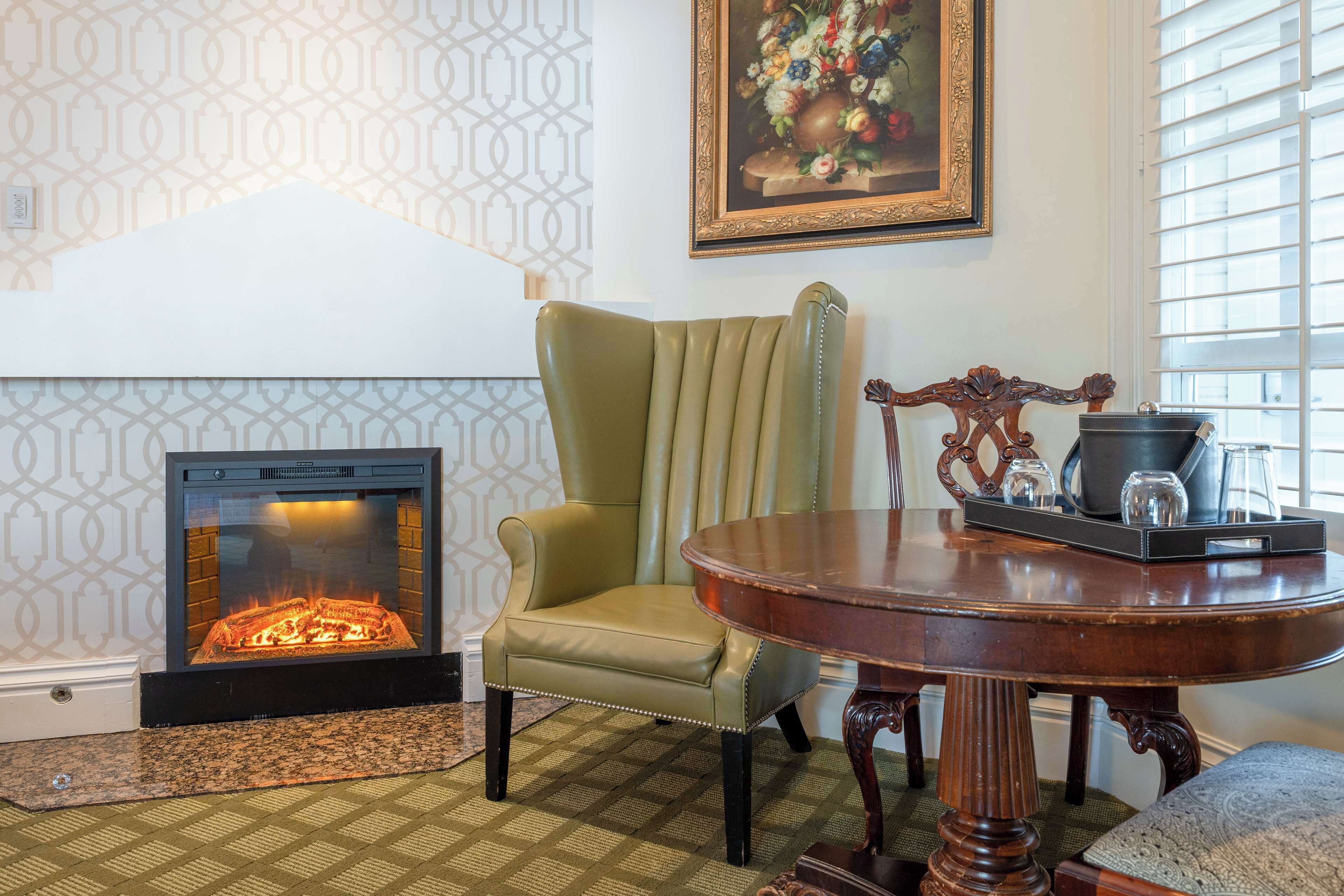 A room with a fireplace, a green upholstered chair, a wooden table with a tray, and a patterned carpet.
