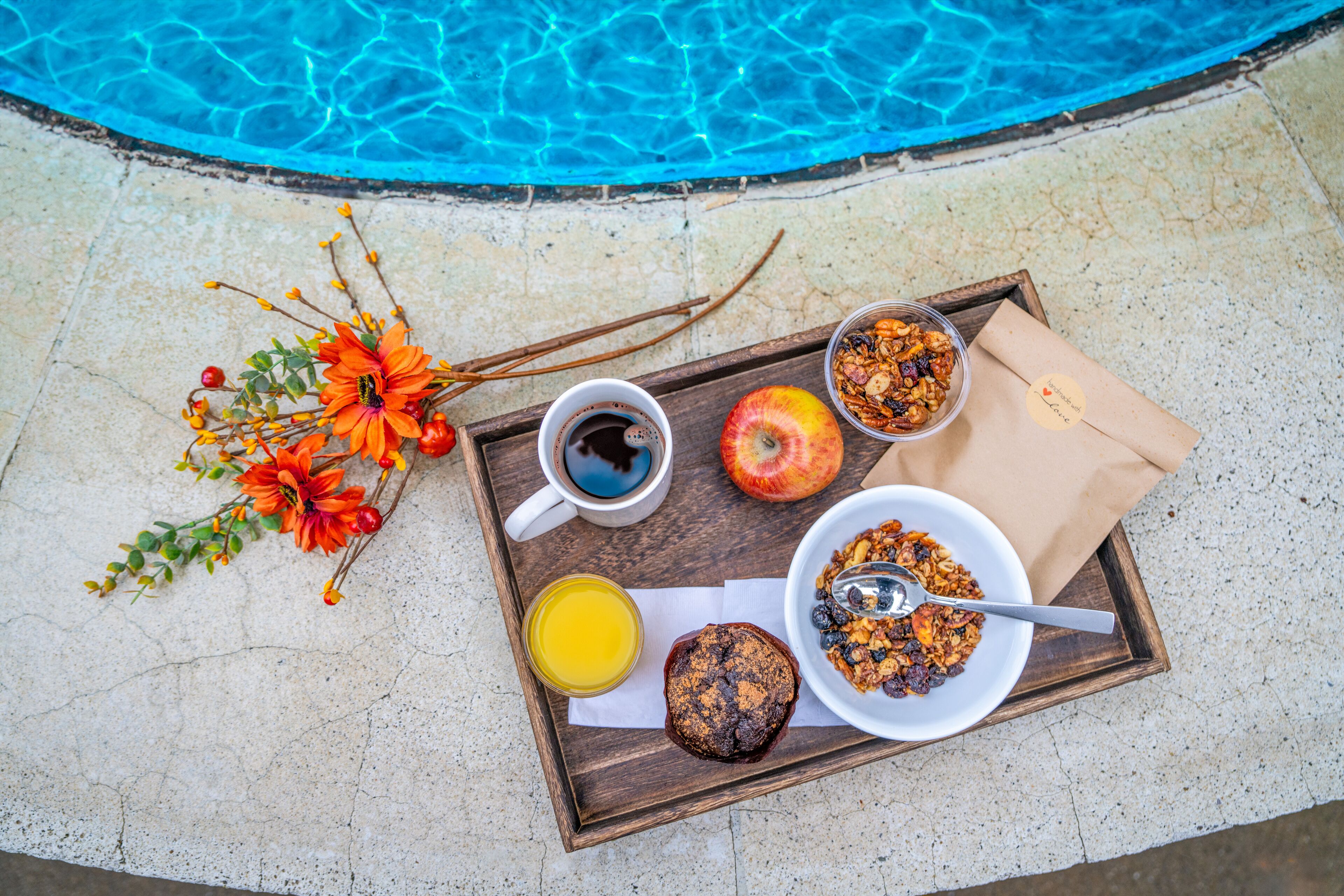 A breakfast tray with coffee, juice, a muffin, and a bowl of cereal by a pool.
