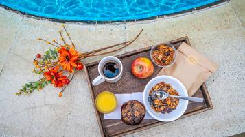 A breakfast tray with coffee, juice, a muffin, and a bowl of cereal by a pool.
