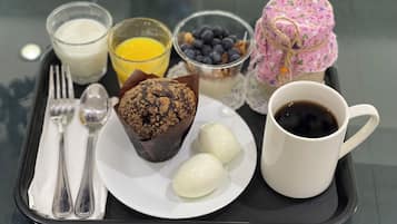 A tray with a muffin, two white eggs, a cup of coffee, a glass of orange juice, a glass of milk, a bowl of blueberries, and a pink container tied with a string.