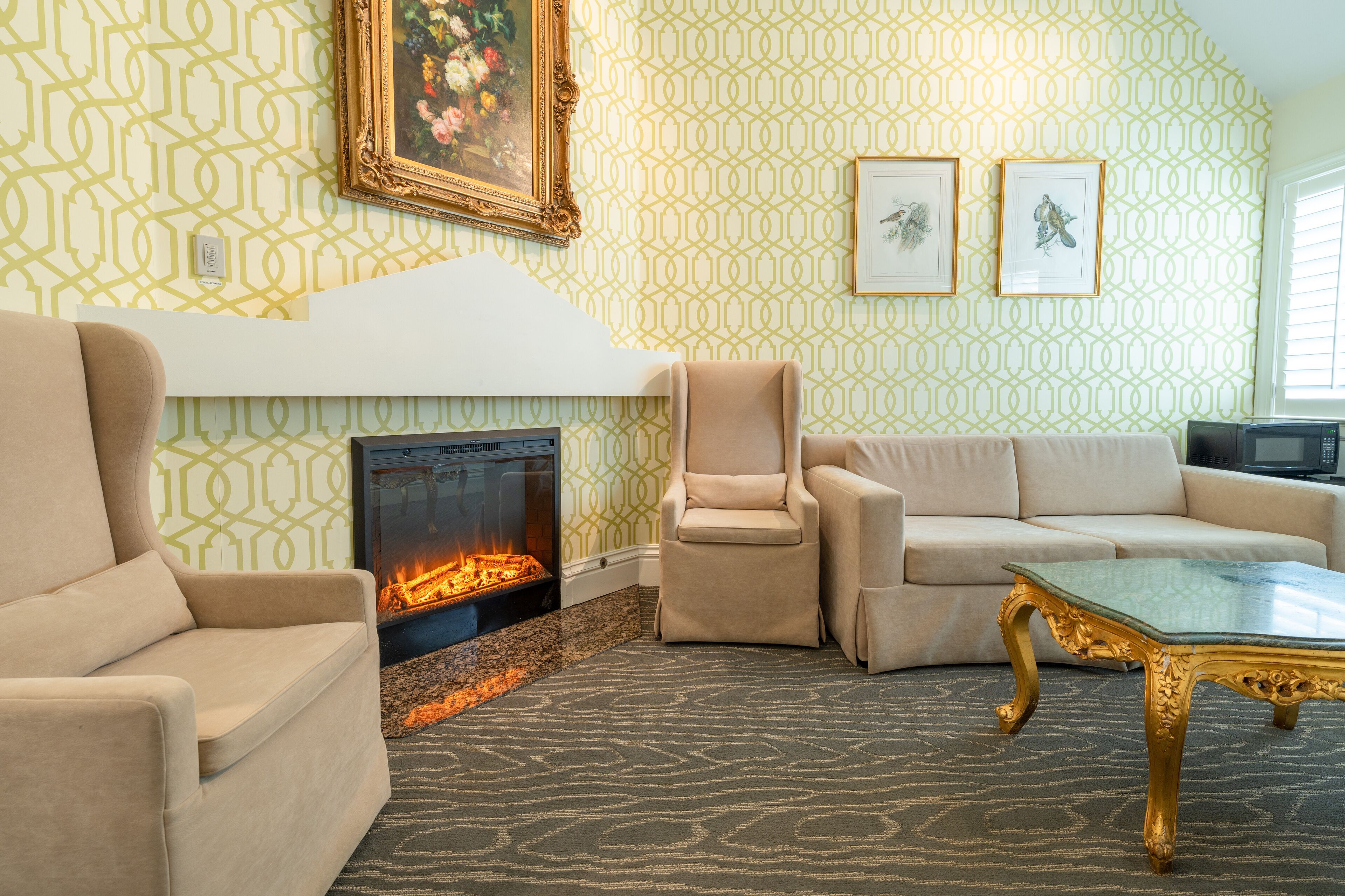 A living room with a fireplace, beige sofas, and a patterned wallpaper.