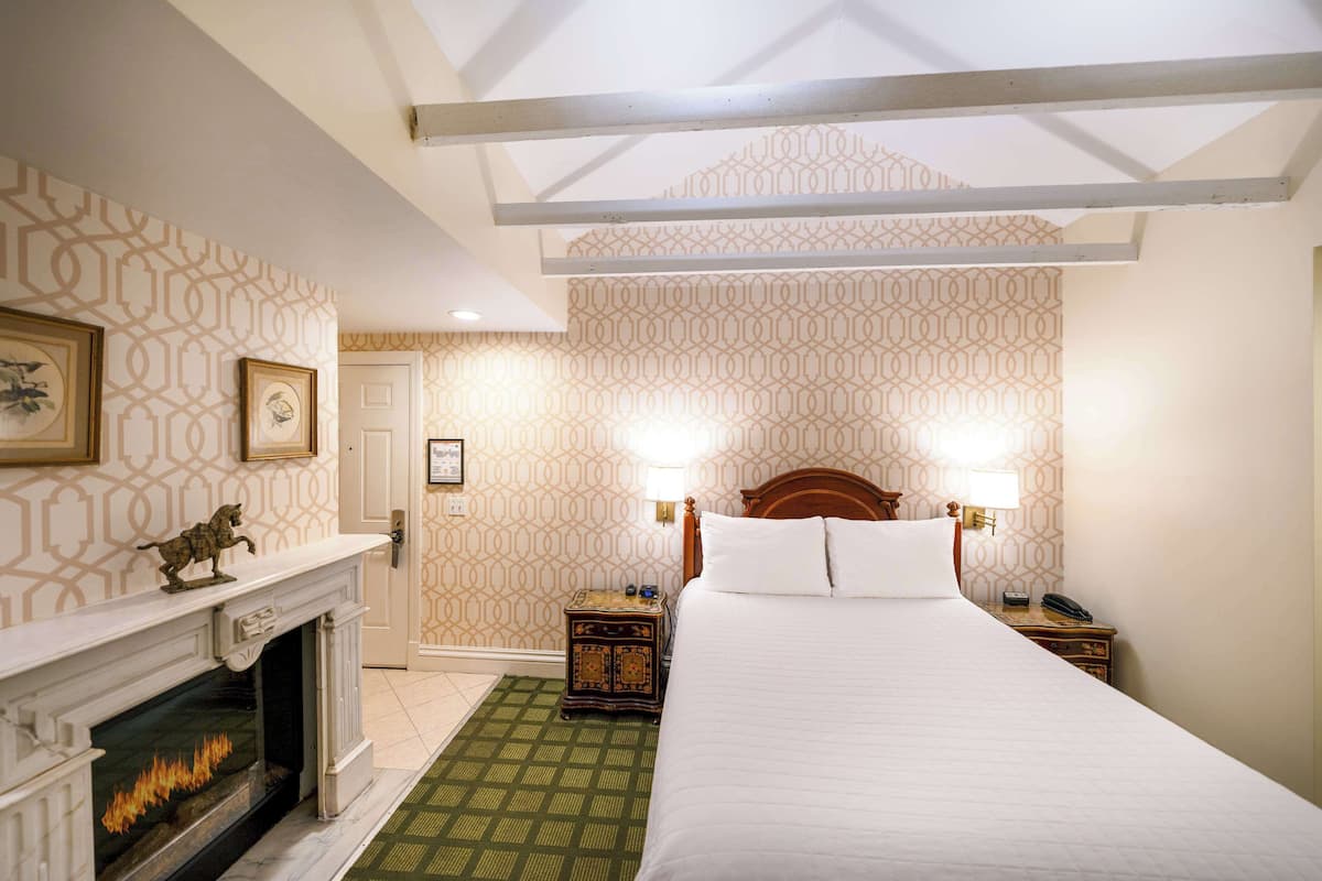 A hotel room with a large bed, a fireplace, a patterned wall, and a green carpet.