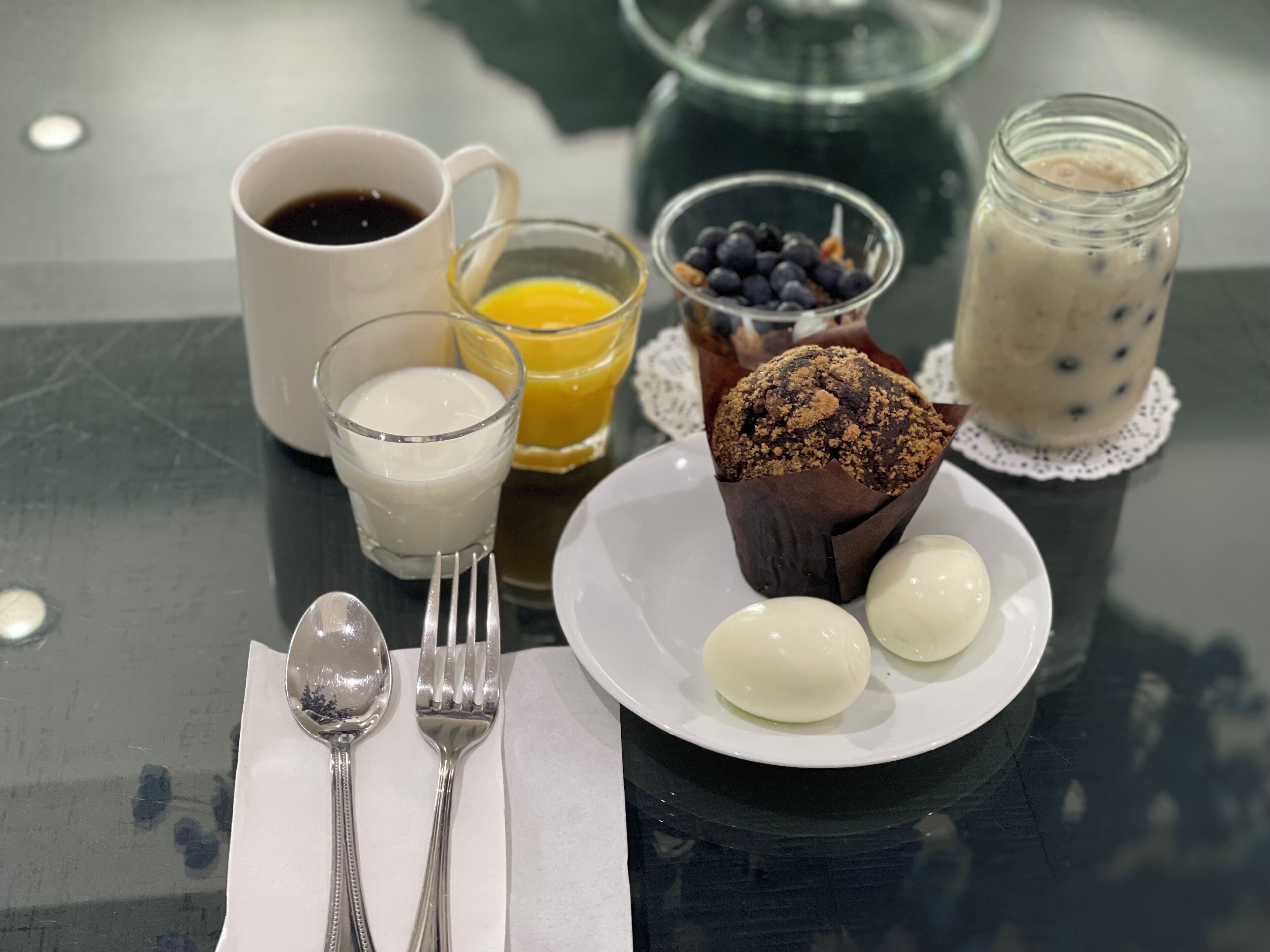 A breakfast setting with a muffin, two eggs, a glass of milk, a glass of orange juice, and a cup of coffee on a table.