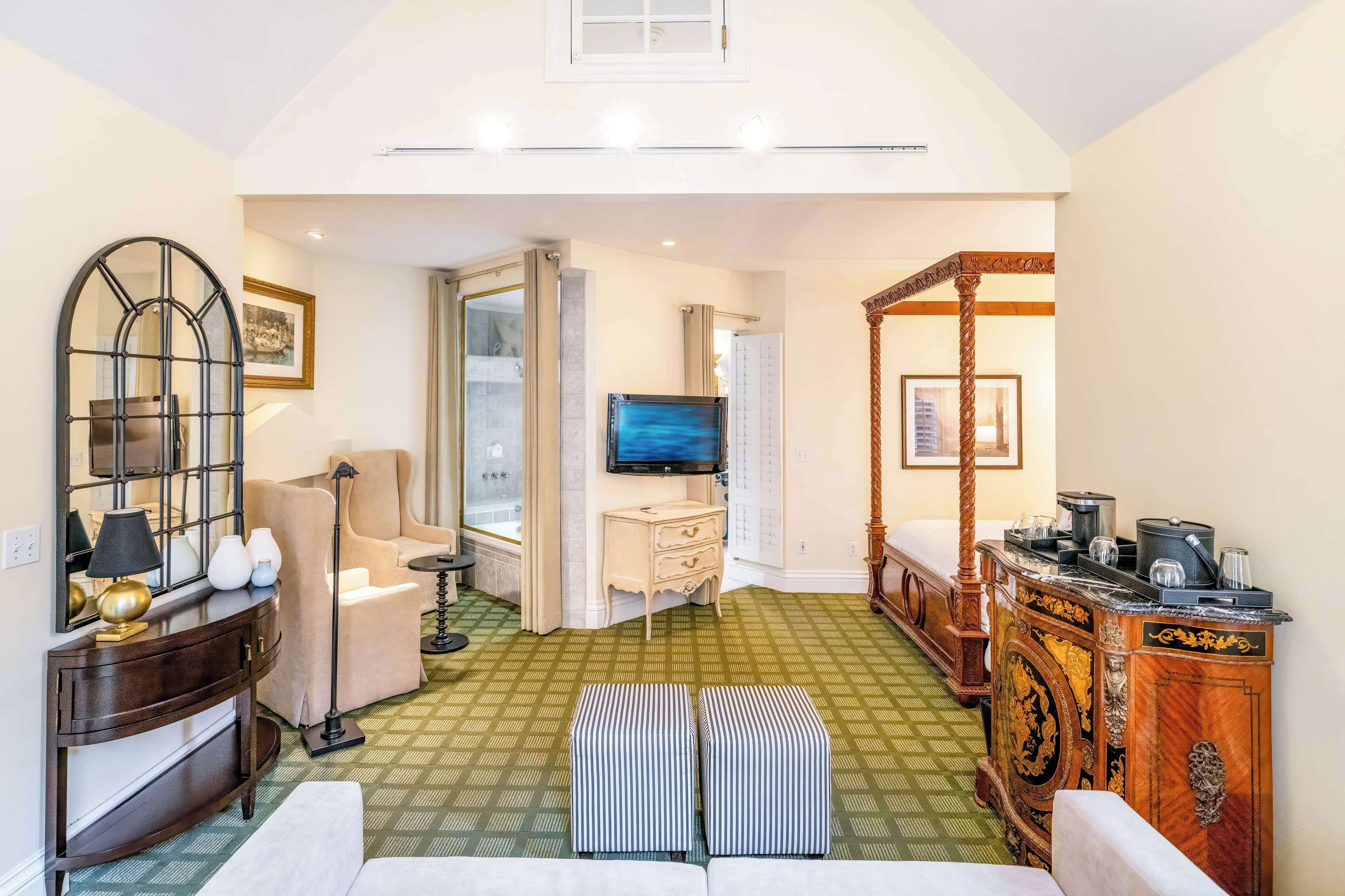 Une chambre d’hôtel avec un sol à motifs verts, un grand miroir, un canapé, une télévision et une armoire en bois.