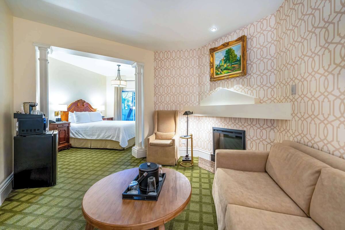 A hotel room with a bed, a sofa, a coffee table, a TV, and a fireplace.