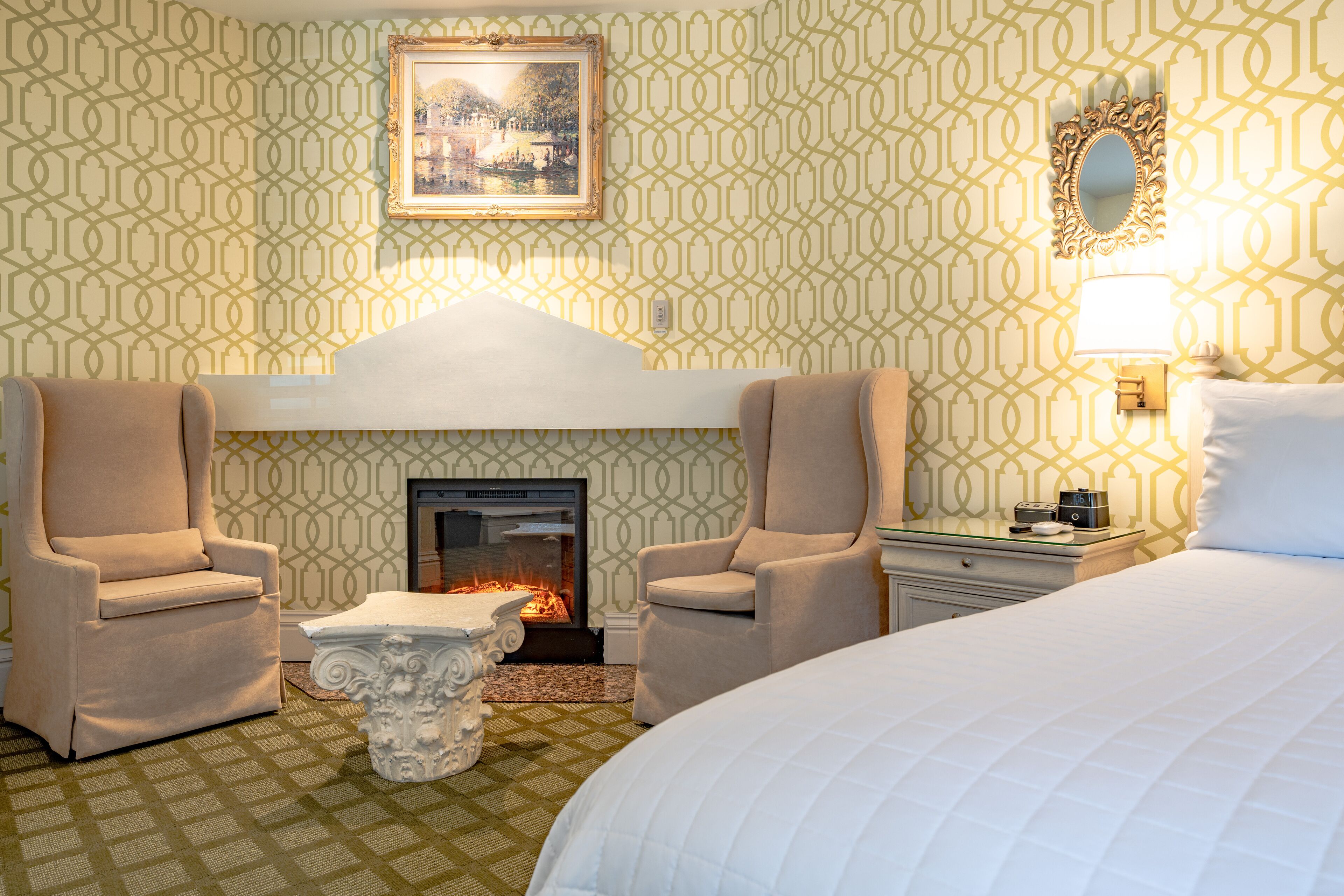 A hotel room with a fireplace, two armchairs, a bed, and a nightstand.