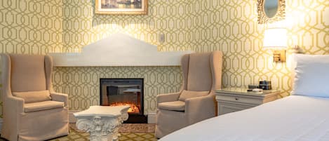 A hotel room with a fireplace, two armchairs, a bed, and a nightstand.