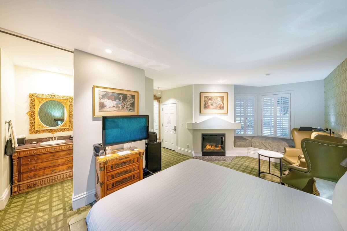 A hotel room with a large bed, a television, a fireplace, a sofa, and a desk.
