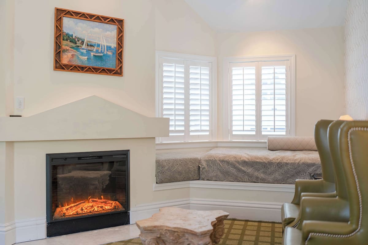A cozy living room with a fireplace, a bench by the window, and a green armchair.
