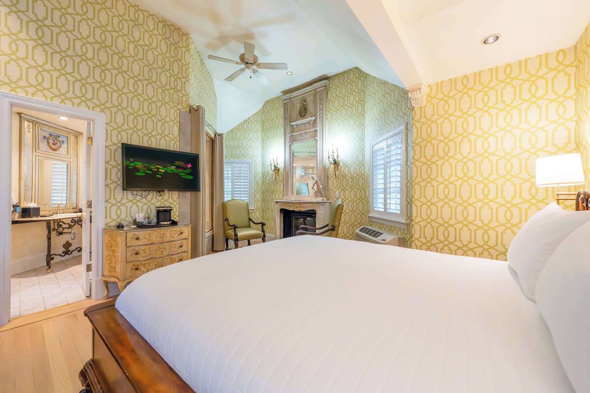 A bedroom with a large bed, a television, a fireplace, and a ceiling fan.