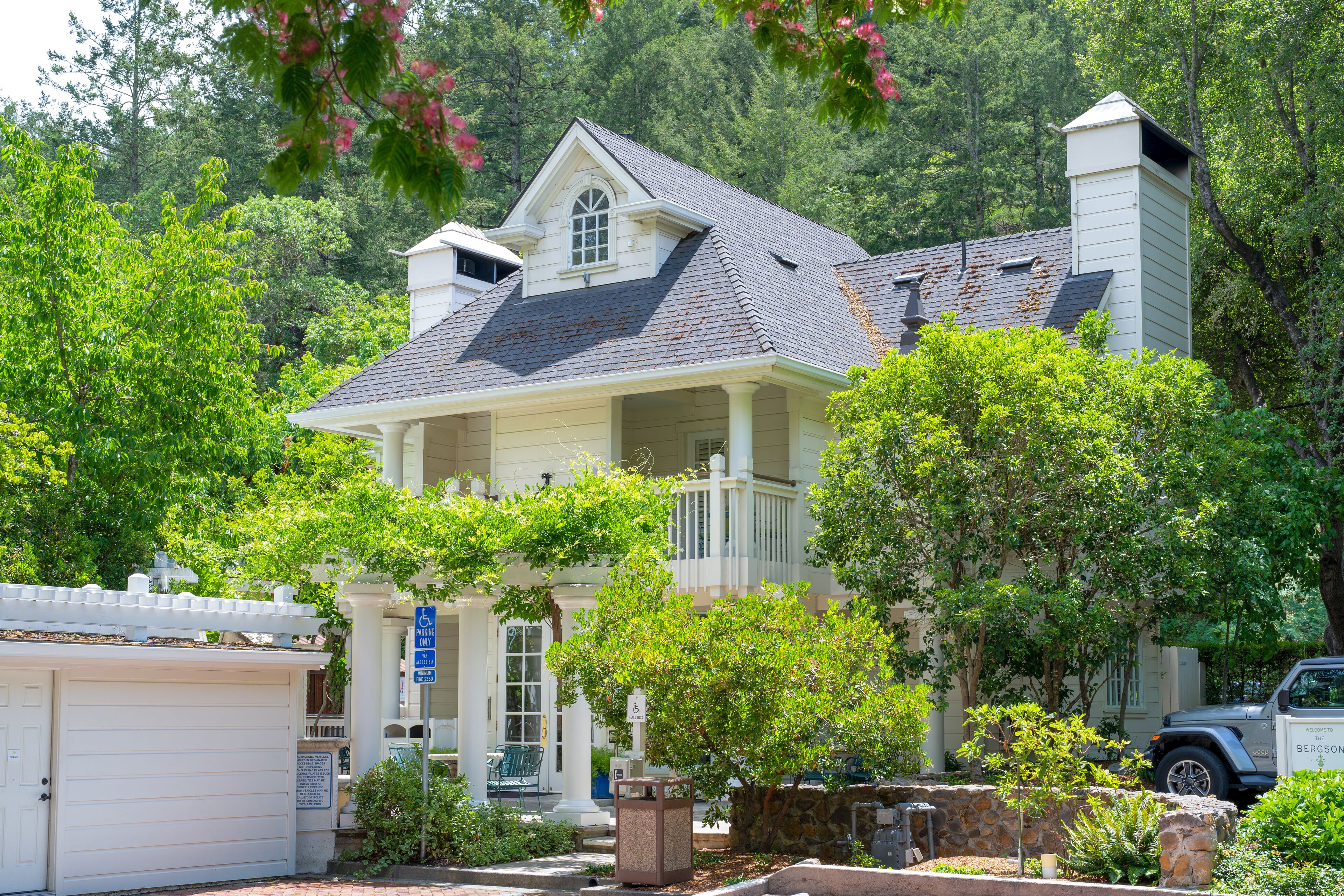 A two-story house with a covered porch, surrounded by lush greenery and trees.