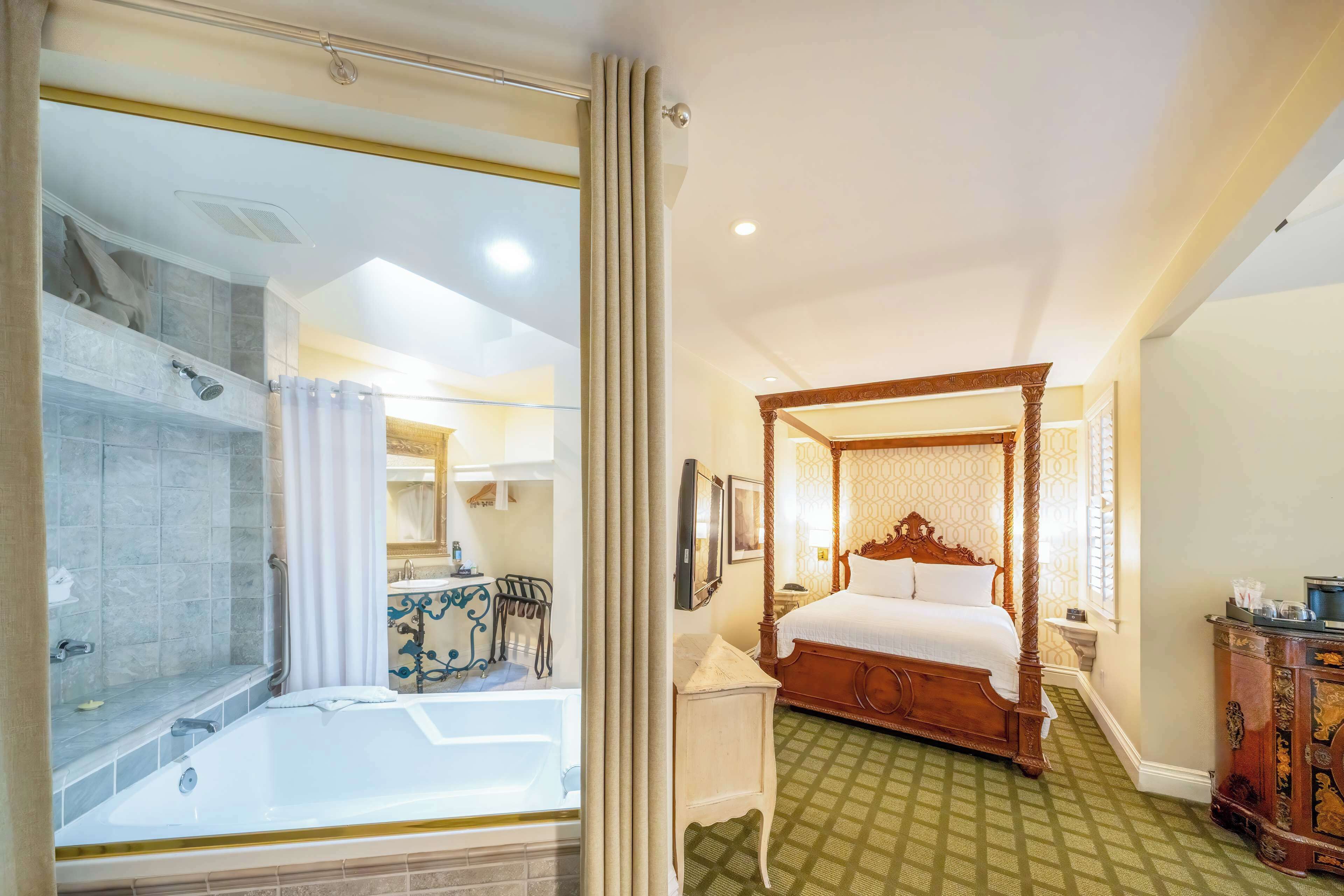 A spacious bedroom with a four-poster bed, a separate bathroom with a bathtub, and a green patterned floor.