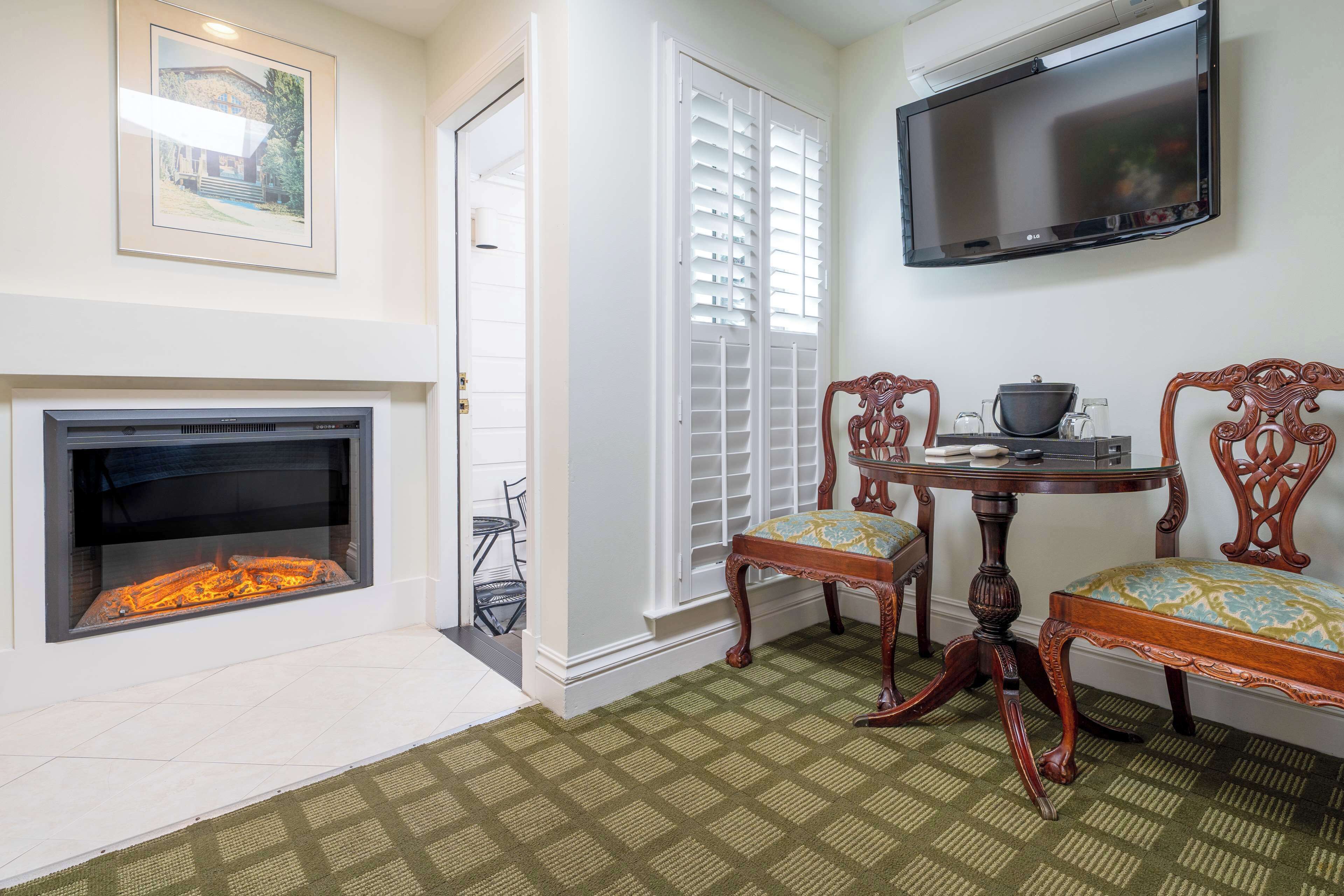 A living room with a fireplace, a television mounted on the wall, and two wooden chairs with cushioned seats.
