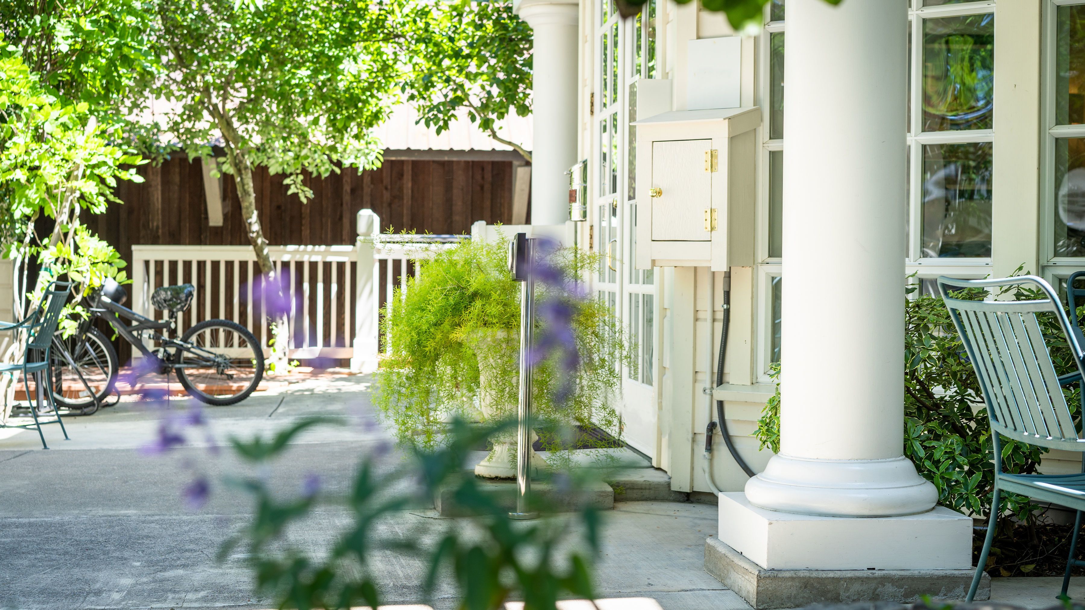 A building with a white exterior, a wooden fence, a bicycle, and a bench.