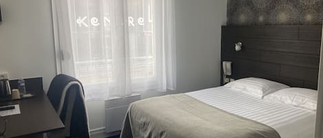 Ein Hotelzimmer mit Bett, Schreibtisch, Stuhl, Telefon und einem Fenster mit Vorhängen.