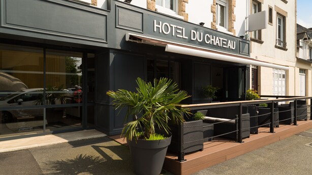 Ein Hotel namens "HOTEL DU CHATEAU" mit moderner Fassade, großen Fenstern und einer Außenbereich-Sitzgelegenheit mit Topfpflanzen.