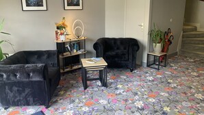 Ein Wohnzimmer mit zwei schwarzen Sesseln, einem kleinen Tisch, einem Bücherregal und einem Teppich mit Blumenmuster.