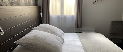 A neatly made bed with white bedding, a headboard with a patterned design, and a chair to the right.