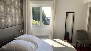 Ein Schlafzimmer mit Bett, Spiegel und Blick auf Grünfläche.