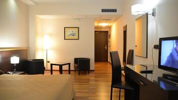 A hotel room with a bed, desk, chair, TV, and a framed picture on the wall.