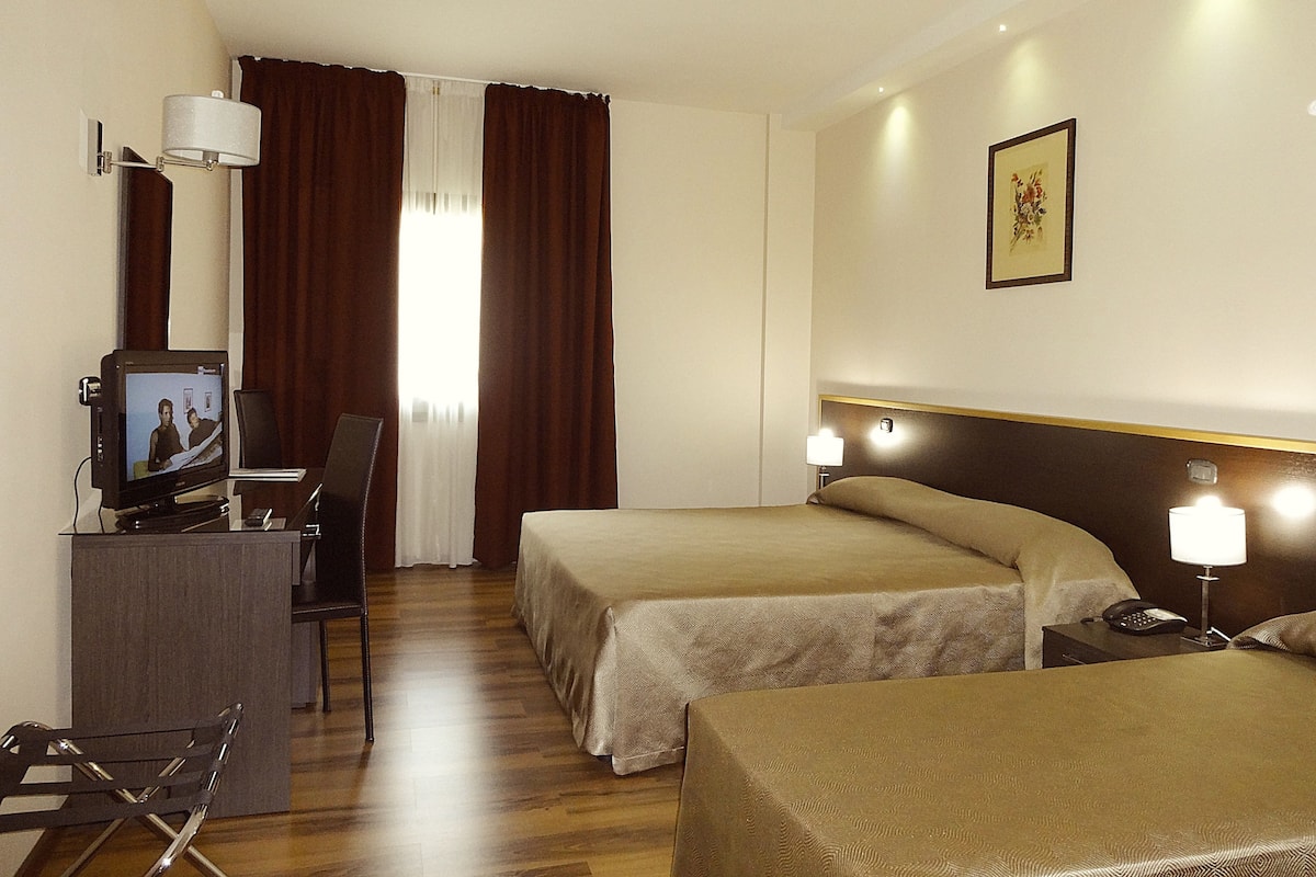 A hotel room with two beds, a desk with a television, a chair, and a desk lamp.
