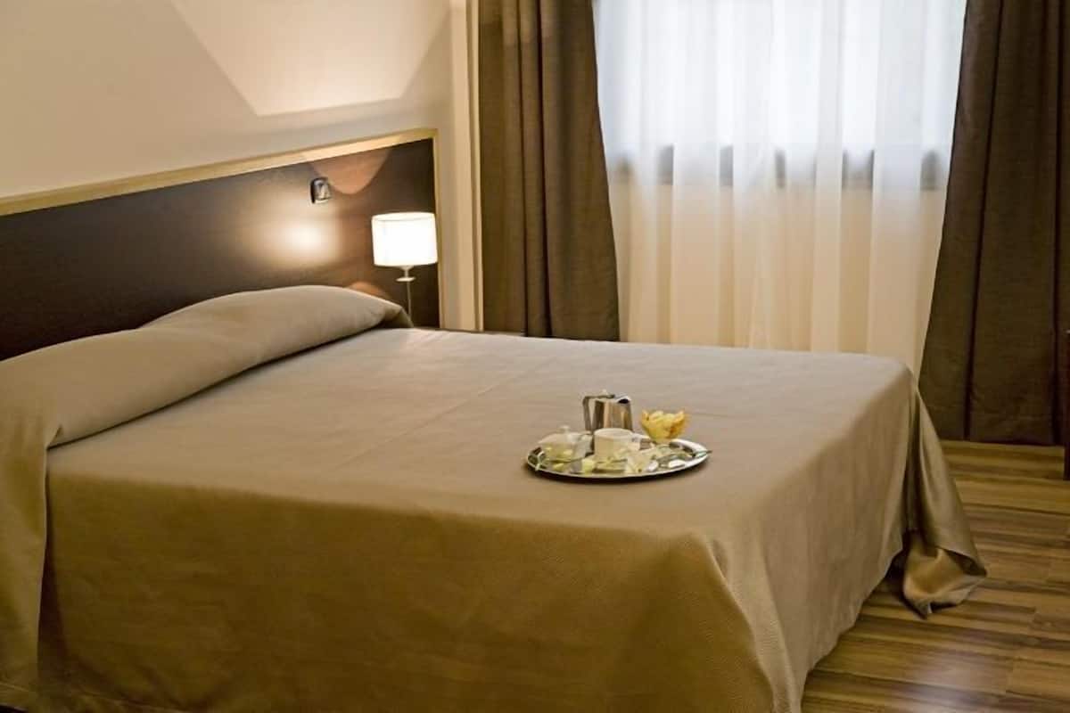 A hotel room with a neatly made bed, a tray with breakfast items, and a television on a wooden floor.