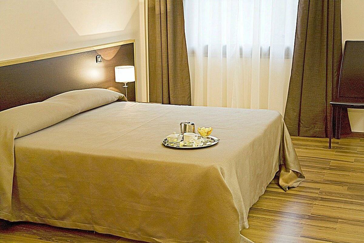 A neatly made bed with a tray of breakfast items, a bedside lamp, and a wooden floor.