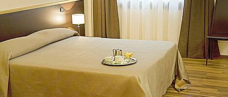 Una cama bien hecha con una bandeja de alimentos para el desayuno, una lámpara de noche y piso de madera.