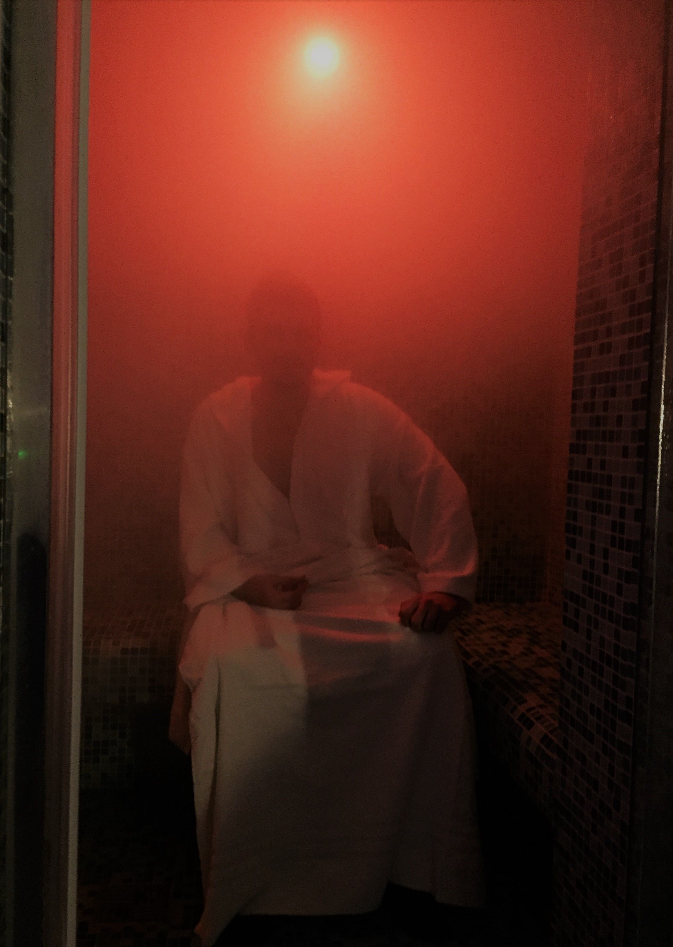 Una persona sentada en una habitación con poca luz, iluminada por una fuente roja en la parte superior.