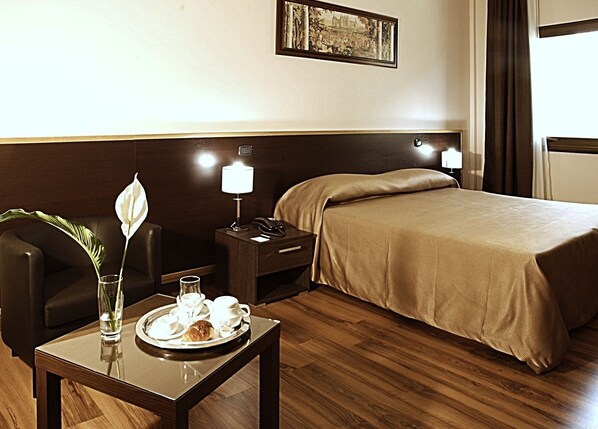 A hotel room with a bed, a nightstand with a lamp, a chair, a table with a tray of breakfast items, and a framed picture on the wall. - Forum Palace Hotel (Cassino)