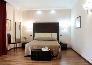 A hotel room with a bed, bedside tables, a chair, and a small table with a lamp. - Forum Palace Hotel (Cassino)