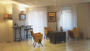 Een hotelkamer met een eethoek, twee gele fauteuils, een tafeltje, een lamp en twee ramen met dunne gordijnen.