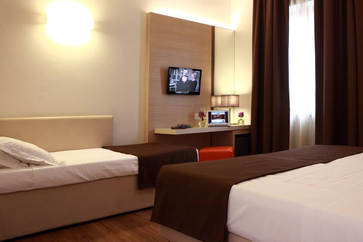 Een hotelkamer met twee bedden, een bureau met een computer, een televisie en een lamp.