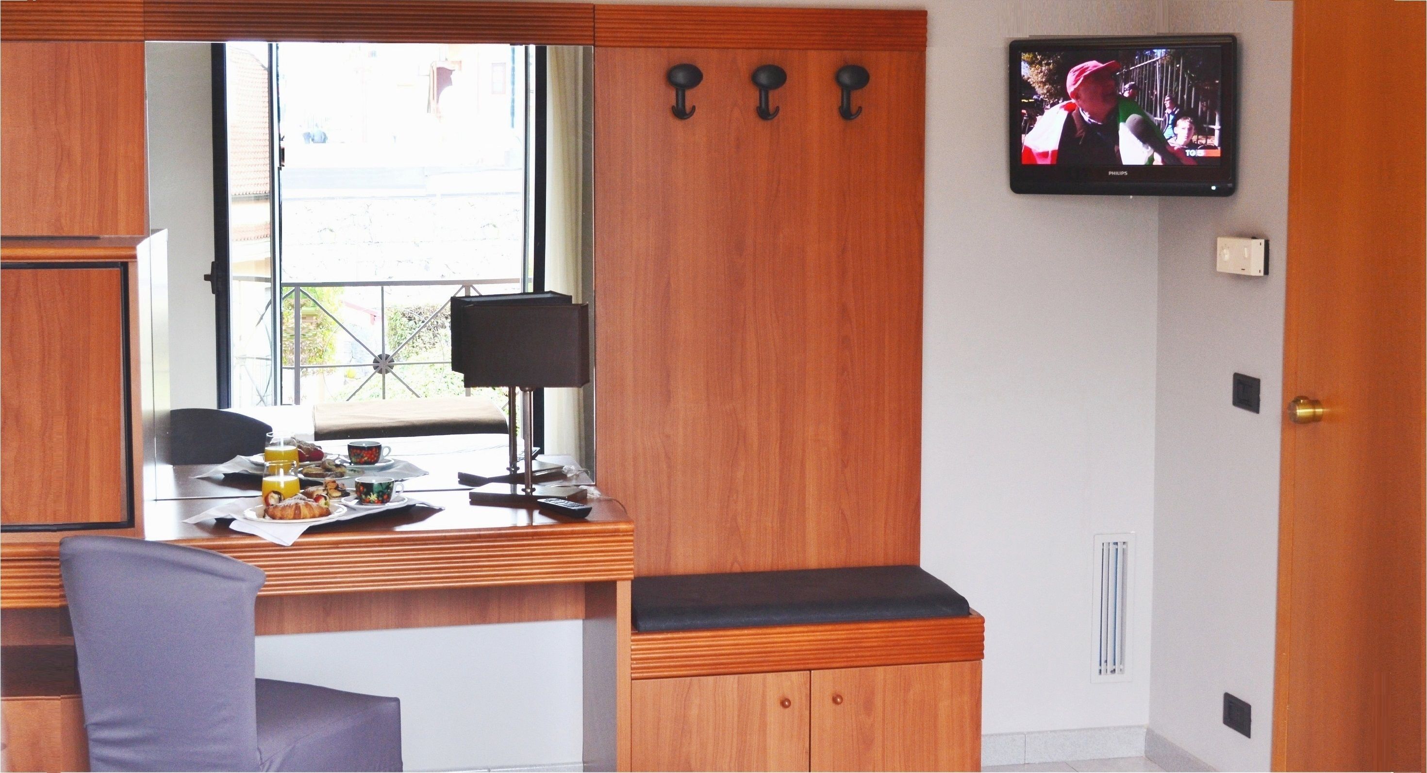 Una habitació amb un escriptori de fusta, una cadira, un televisor penjat a la paret i una finestra amb vista a l'exterior.